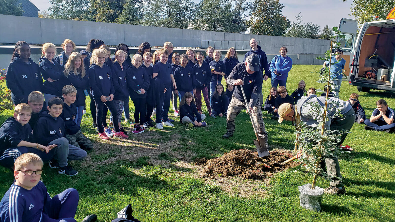 group of school children watching a tree being planted