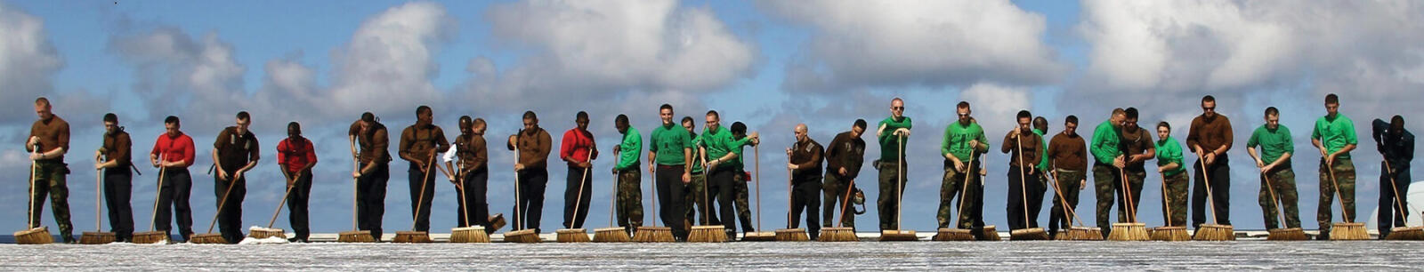 long line of workers cleaning up with brooms and various tools