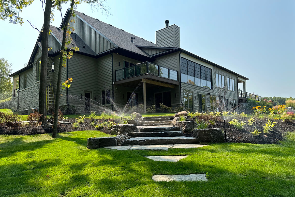 A house on a hill of grass with natural stone steps and irrigation sprinklers running